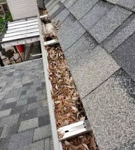 Eavestrough packed with wet leaves and shingle grit before gutter guards